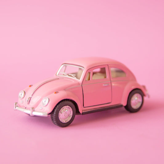 On a pink background is a pink beetle car toy.